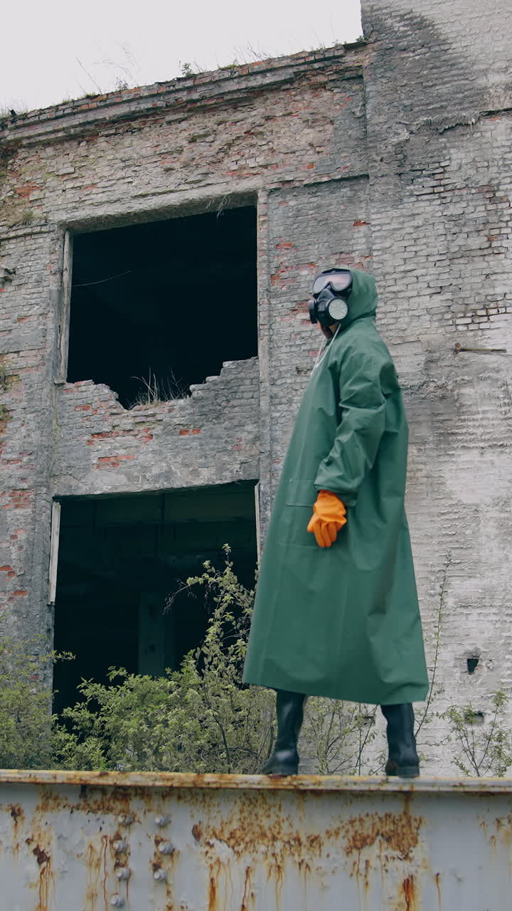 Man in protective clothes in abandoned place. Man in safety suit standing alone on the background of ruined buildings. No people. Apocalypse concept. Vertical video