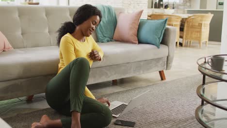 video of happy african american woman sitting on floor using laptop