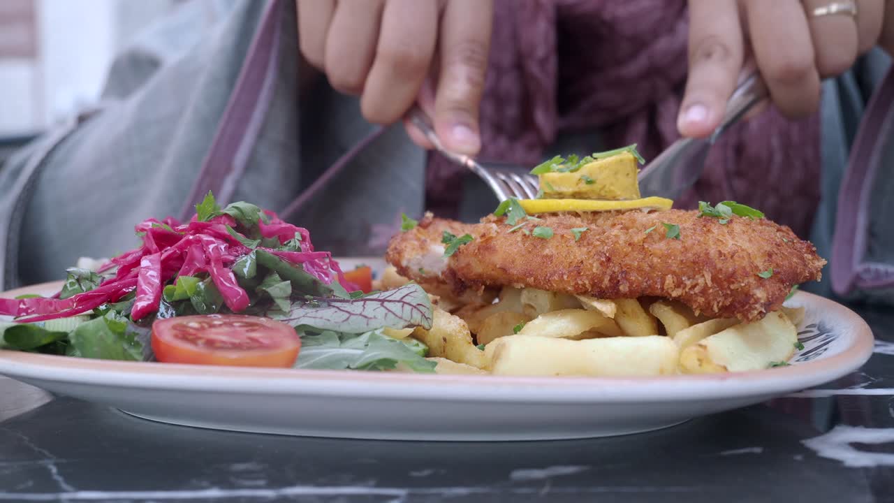 A person enjoying a meal of fried fish, french fries, and salad