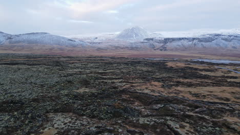 Aerial-shot-of-a-lava-field-in-front-of-mountains-in-Iceland