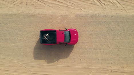 Red-truck-parked-on-flat-sandy-desert-track,-top-down-view