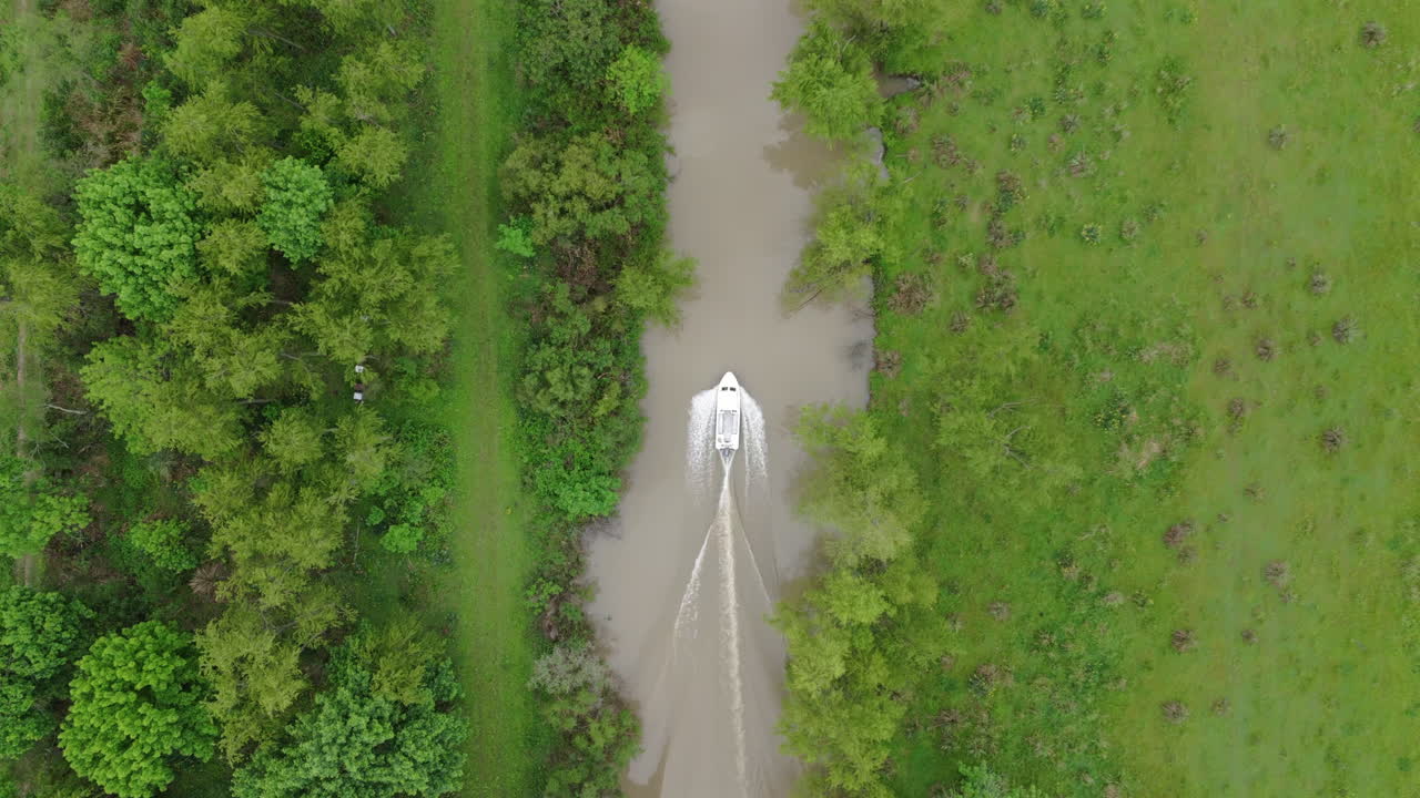 A small motorboat moves through a narrow river channel, surrounded by dense green vegetation.