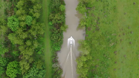 a small motorboat moves through a narrow river channel, surrounded by dense green vegetation.