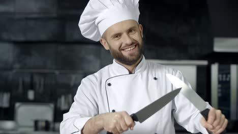 hombre chef divertirse con cuchillos en la cocina. chef sonriente afilando cuchillos cruzados
