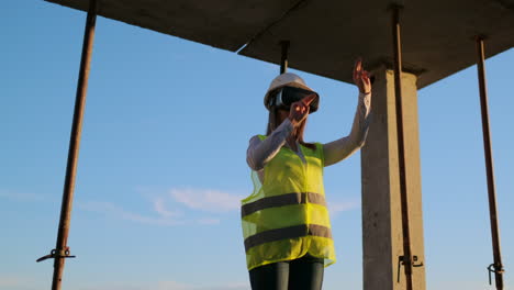 a woman engineer at a construction site in virtual reality glasses moves her hands simulating the work of the interface of the future at sunset