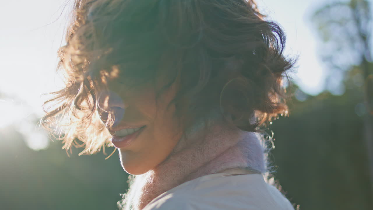 숲에서 빛을 즐기는 곱슬머리 여성은 조용한 고독을 클로즈업으로 묘사합니다.