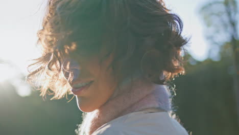 mujer de cabello rizado disfruta de la luz del sol en el bosque retratando la tranquila soledad en primer plano