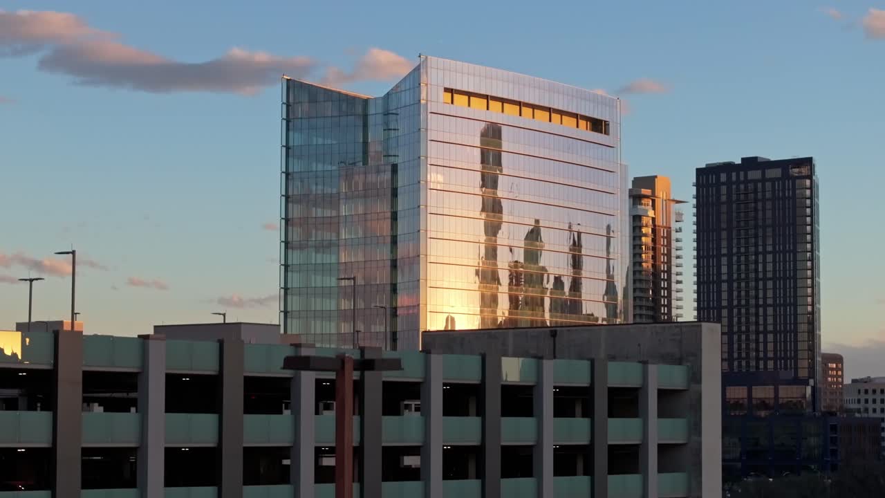 A zoomed in drone shot with parallax increasing elevation and centered on a parking garage and a building near the University Medical Center in Austin Texas with sunset reflecting off the windows