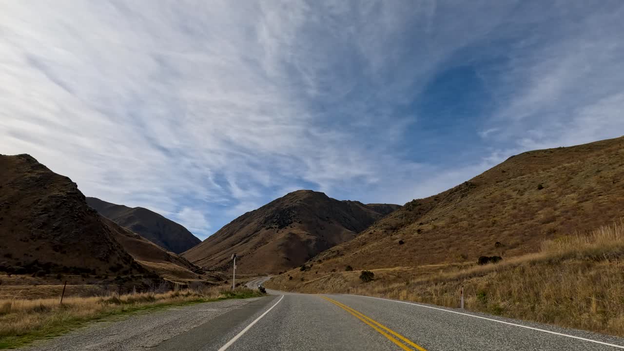 A serene drive through Queenstown's mountainous landscape in autumn, showcasing winding roads, clear skies, and vibrant foliage