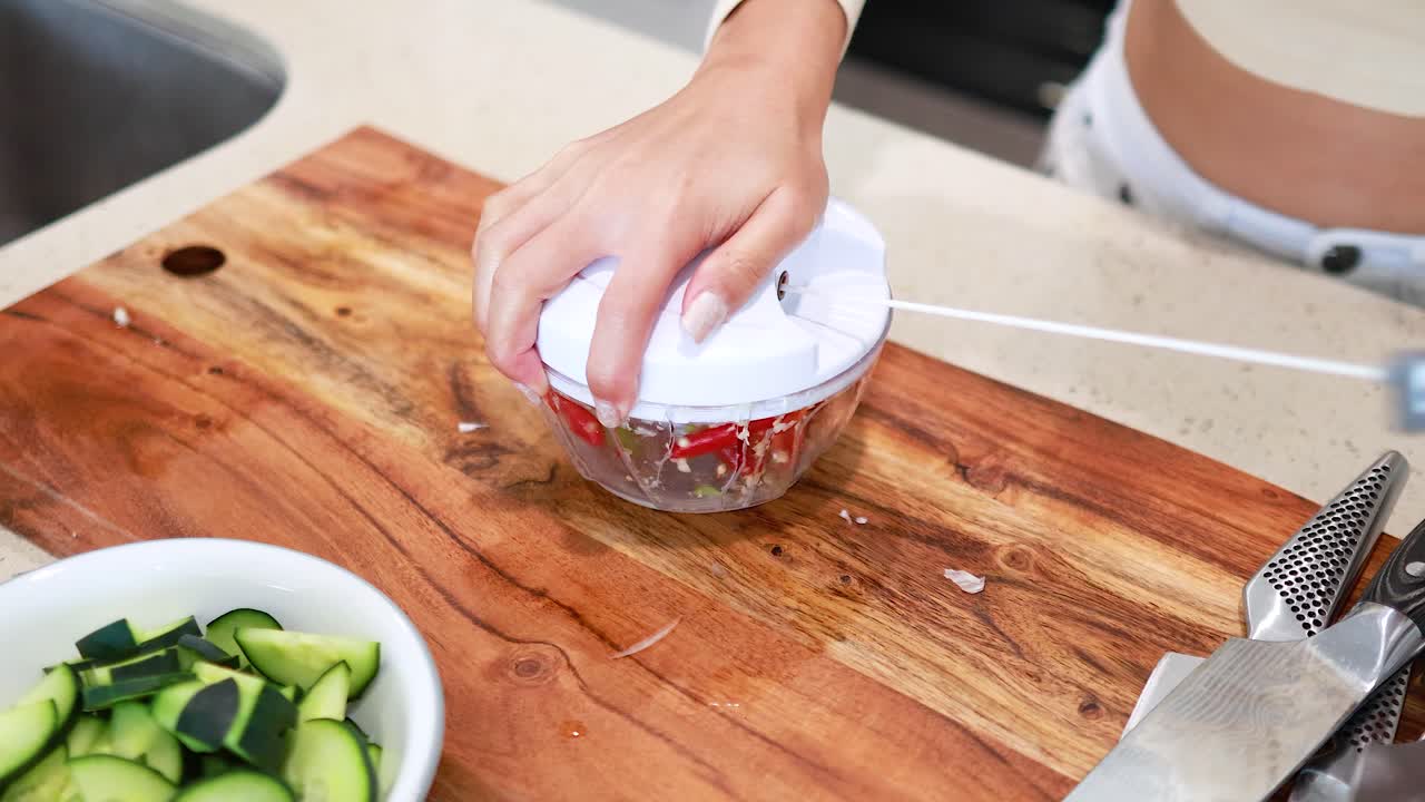 Hands using a manual chopper to prepare garlic on a wooden board. Bright kitchen setting with natural lighting