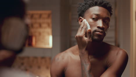 handsome black man looking in bathroom mirror and applying shaving cream