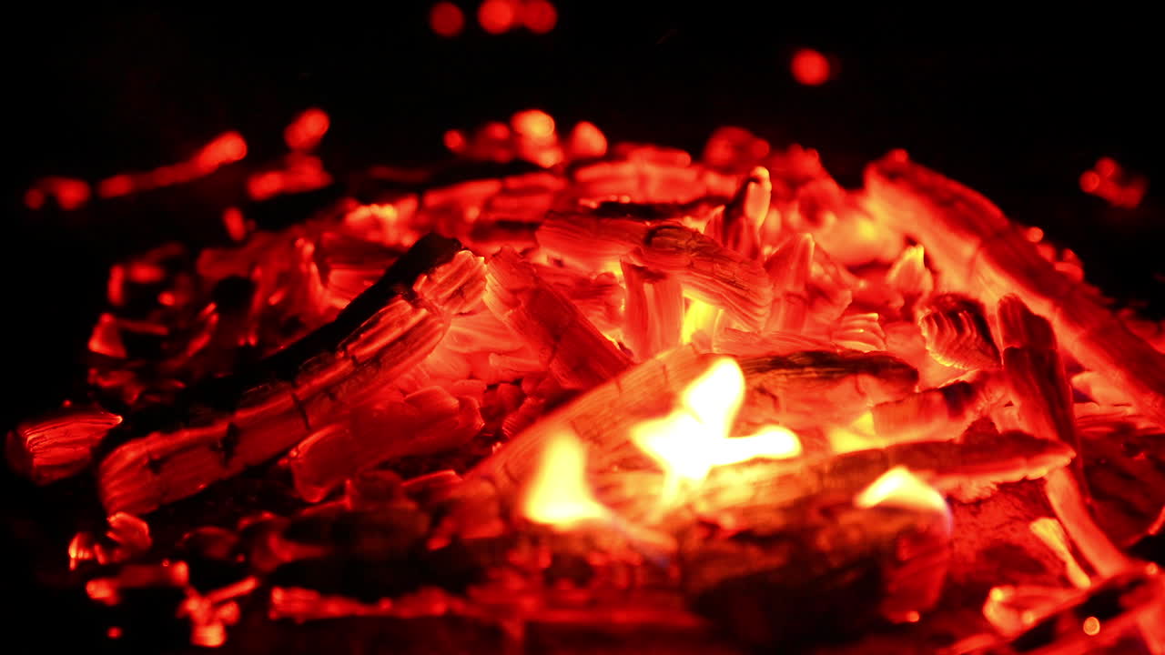 Blowing on the hot embers in the campfire. Red tiny sparks fly up into the darkness. Close up.