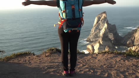 excited female backpacker standing at rocky cliff