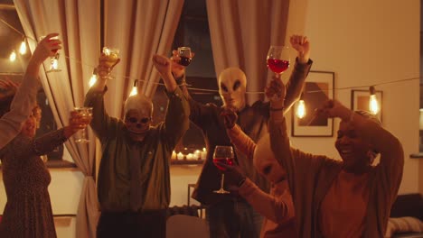 masked friends dancing with wine at halloween party