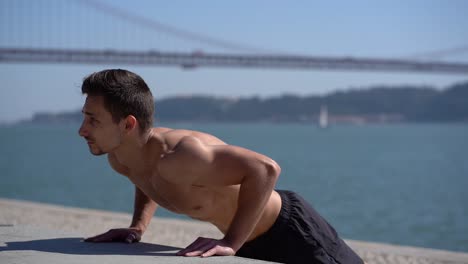 Focused-bare-chested-man-doing-push-ups-at-riverside