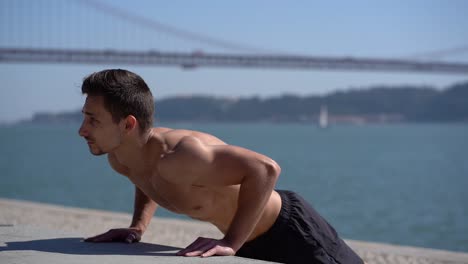 focused bare-chested man doing push ups at riverside