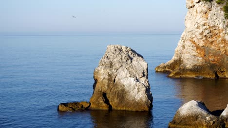 Acantilado-Rocoso-En-El-Mar-Adriático,-Con-Gaviotas-Volando-En-El-Fondo