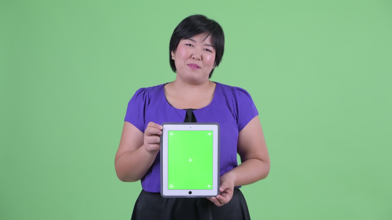 초록색 배경에 디지털 태블릿에서 크로마 키를 보여주고 미소 짓고 짧은 헤어 스타일을 가진 과체중 아시아 여성의 초상화
