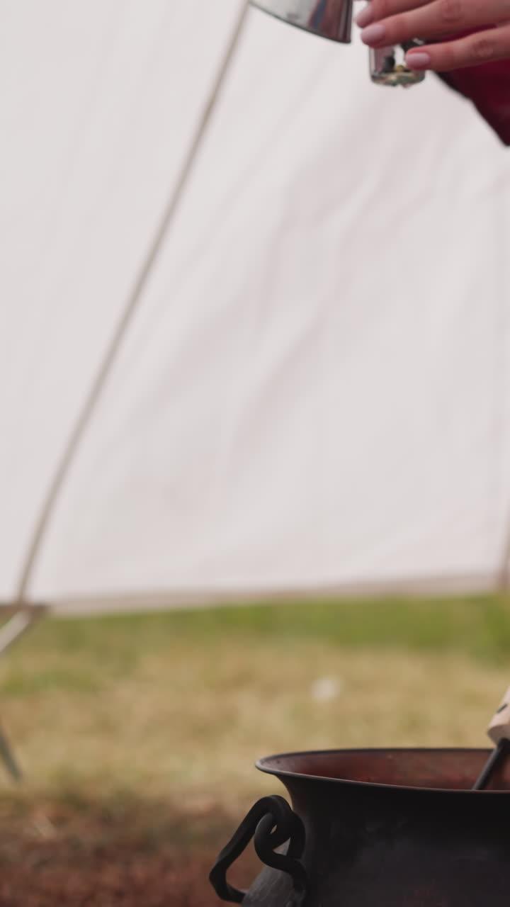 여성 마법사는 작은 유리 병에 마법의 약을 부어주고, 여성은  텐트 근처의 테이블에 앉아있는 비에서 음료를 만들고, 중세 시대의 마법사의 활동.