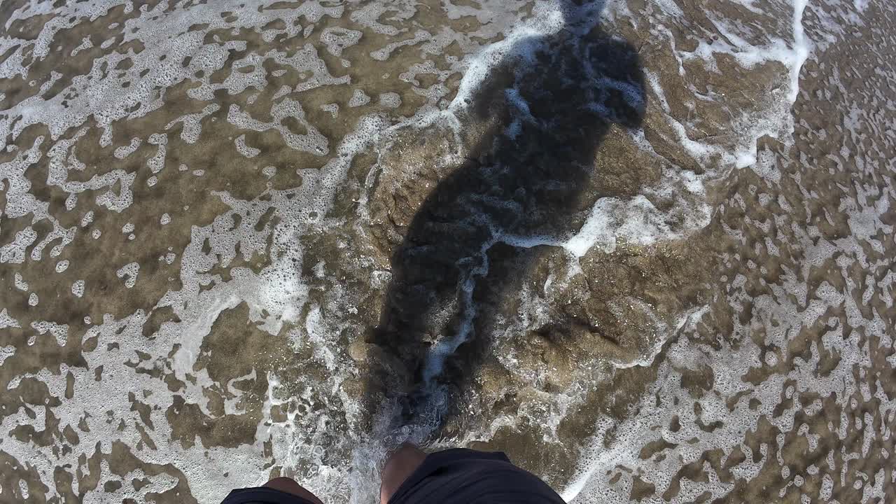 Shadow of a person walking along Polzeath Beach in Cornwall on a bright, sunny day. The smooth sand, clear shadows, and footprints create a peaceful and serene coastal ambiance