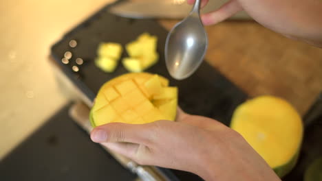 close up of female hands scooping chunks of mango