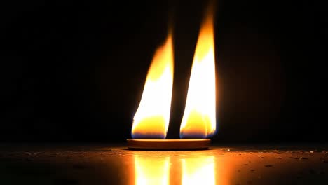 a lit candle in the dark with a reflection on the floor