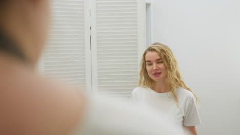 client with long blonde hair walks into salon and smiles while looking at technician partially visible in foreground. bright white interior and louvered doors create clean modern setting