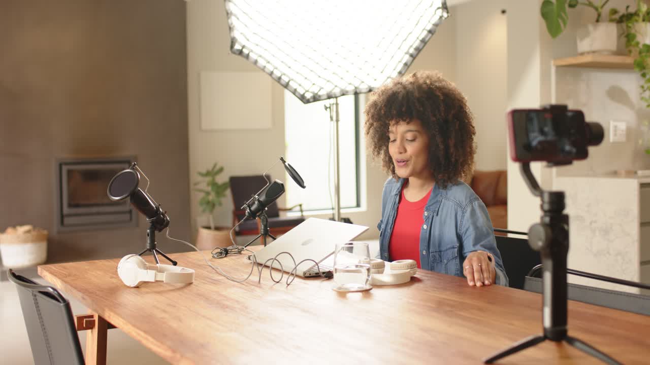 Entering African American woman sitting at home table speaking into microphones and showing laptop