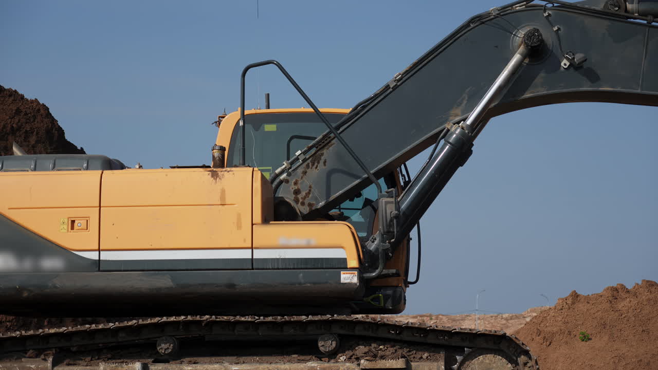 Close-up of a large yellow excavator on a construction site with dirt piles