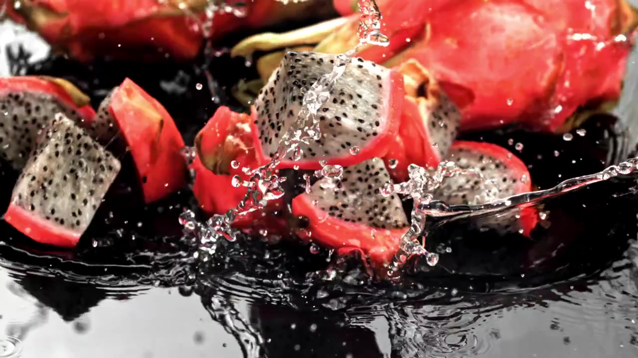 Frische Drachenfruchtstücke spritzen in Zeitlupe ins Wasser.
