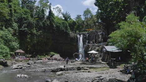 volar a través del cañón con la cascada de tegenungan y numerosos turistas reunidos en su parte inferior