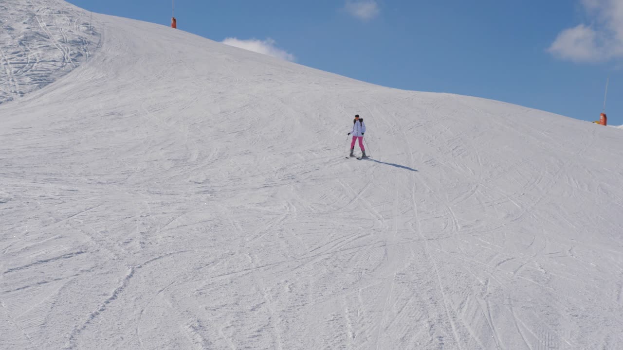 시작하고 불안한 여성 스키 선수가 산 경사 아래로 스키를 타고 있습니다.