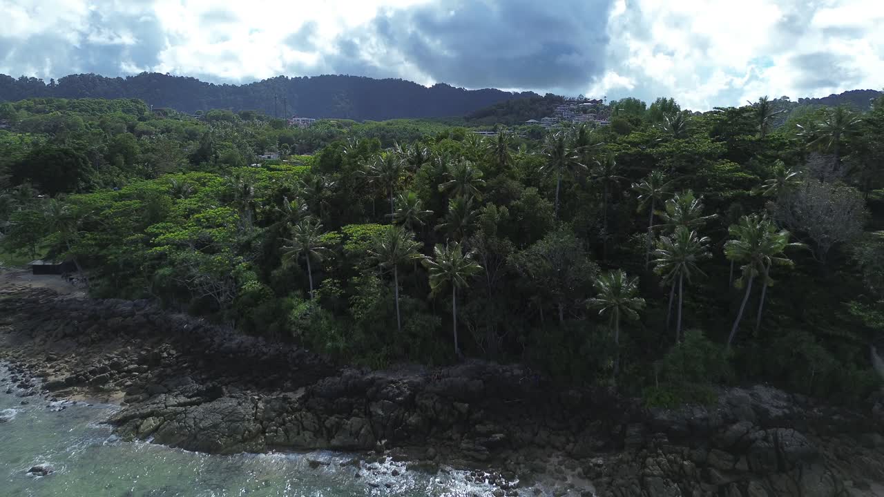 Aerial drone footage of a dense palm forest along a rocky shoreline on Koh Lanta island in Thailand featuring crystal clear turquoise water, small coves and lush tropical coastal scenery