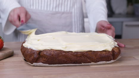 female baker spreading white frosting on carrot cake with spatula