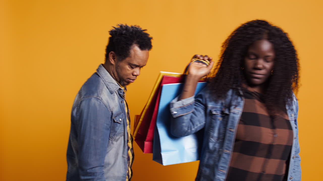 아프리카계 미국인 남자가 쇼핑 가방을 들고 아내를 따라가고 있다