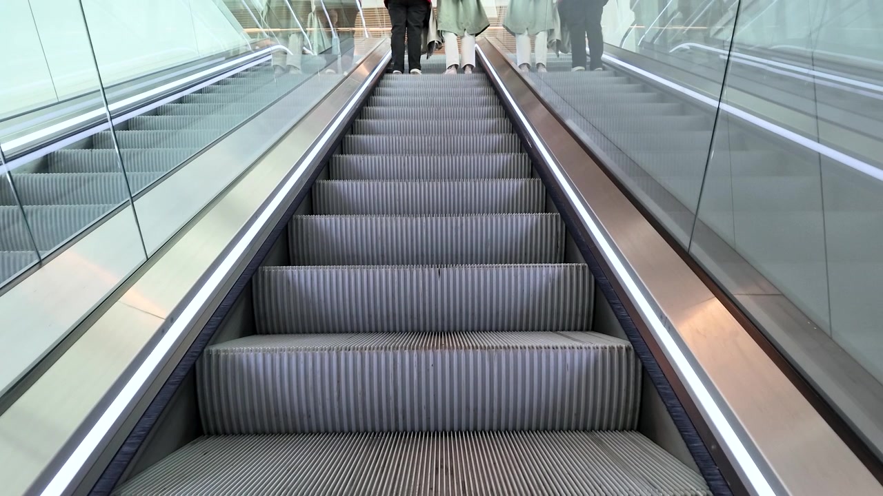Pengambilan gambar sudut rendah orang-orang menaiki eskalator ke atas di stasiun transit bawah tanah modern.