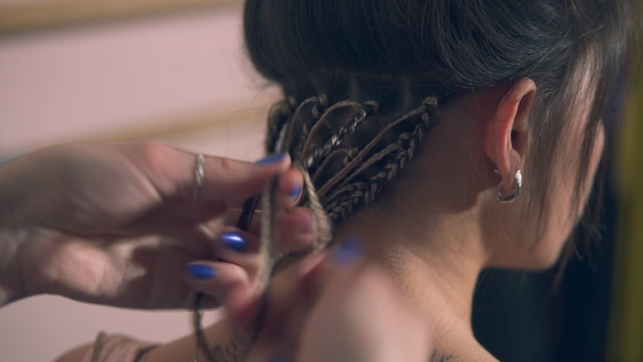 Closeup view of the hairdresser's hands doing dreads for a young woman in the hair salon. Shot in 4k