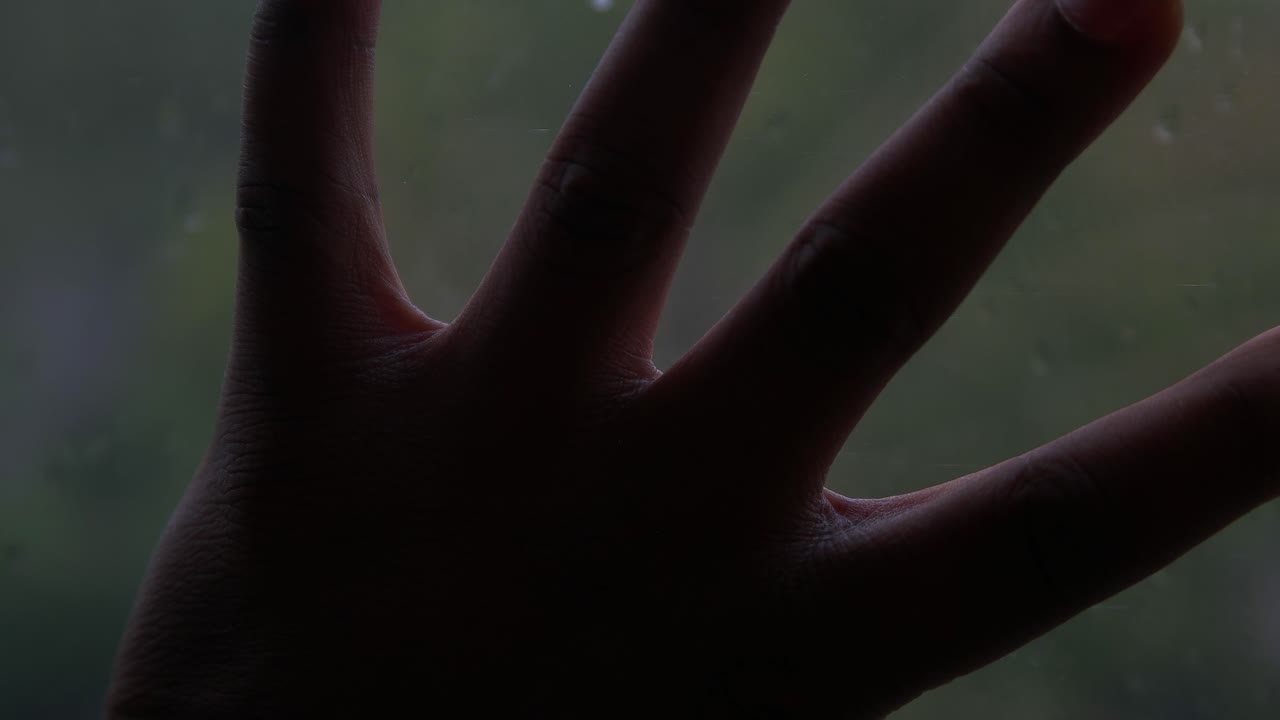 mano negra en la ventana lloviendo y horror de fondo verde