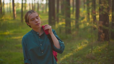 hiker walking through serene forest, adjusting red backpack strap on shoulder, gazing thoughtfully into distance with warm sunlight casting gentle glow on face