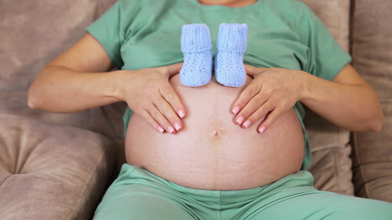Donna incinta che si tocca la pancia. Primo piano di donna incinta seduta sul letto