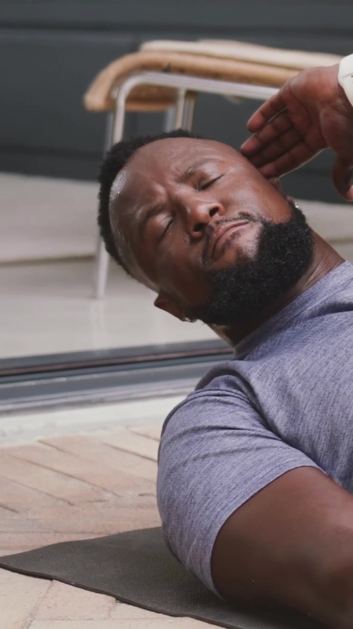 Vertical video: Starting man in grey tee doing oblique crunches on mat for abs by glass door
