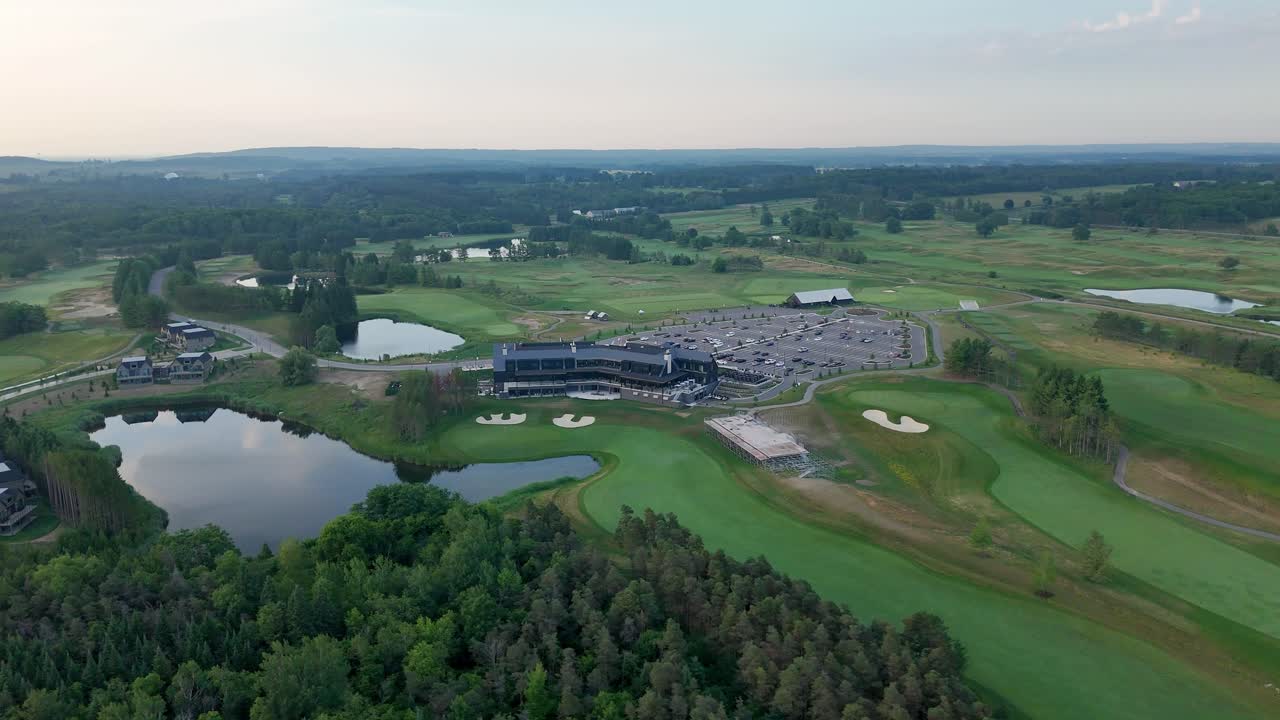 A stunning aerial drone shot orbiting the TPC Toronto at Osprey Valley golf course in Caledon, Ontario, during the golden hour, showcasing its modern clubhouse and pristine fairways