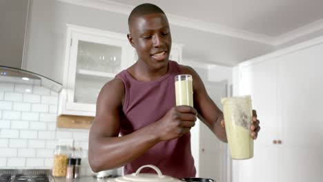 happy african american man drinking healthy smoothie in kitchen at home, slow motion