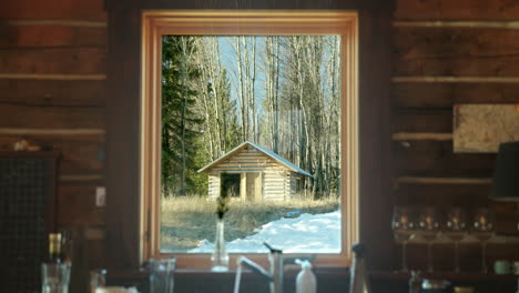 Vista-Interior-De-La-Ventana-De-La-Cabaña-De-Troncos-De-Otra-Pequeña-Cabaña-Al-Amanecer