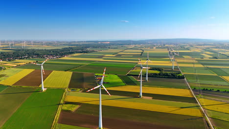 wind turbines produce energy outdoors. wind turbines stand tall over expansive fields of varying crops under a clear blue sky during daylight