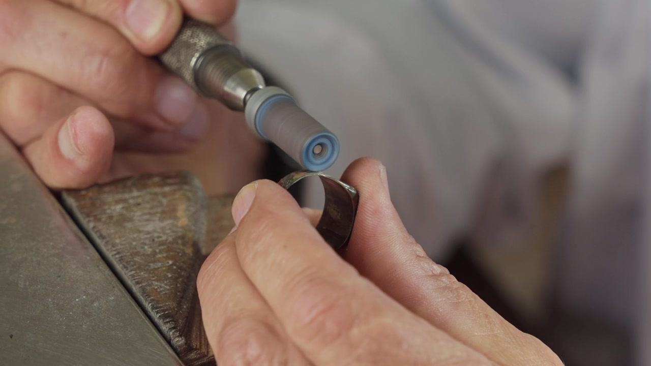 Jeweler hands finishing gold ring with rotary tool and abrasive rubber wheel close up