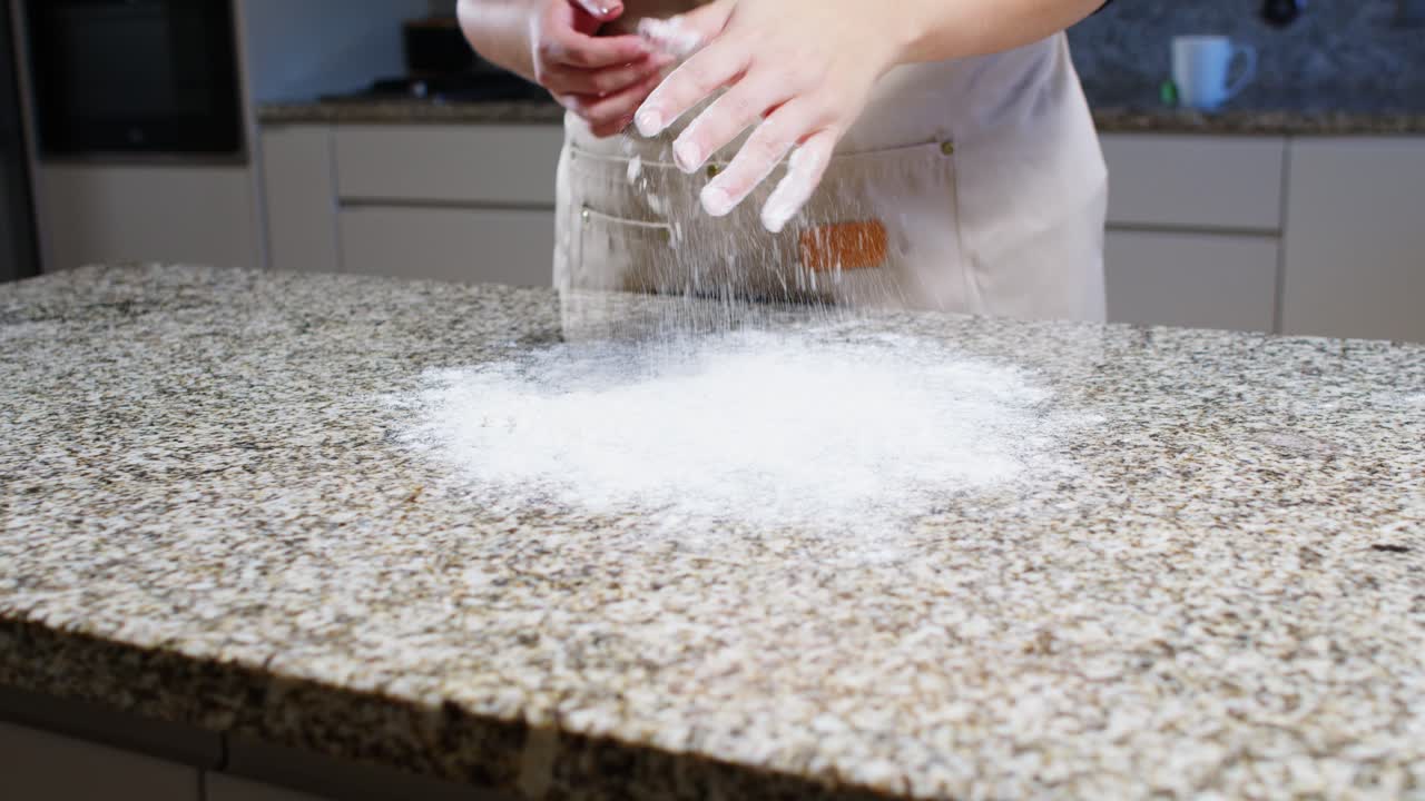 Hands dusting flour on a granite countertop in a kitchen, soft handheld shot.