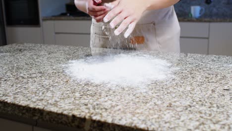 hands dusting flour on a granite countertop in a kitchen, soft handheld shot.