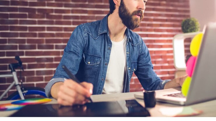 Video di uomo creativo caucasico che usa una tavoletta grafica digitale e un laptop in un ufficio moderno