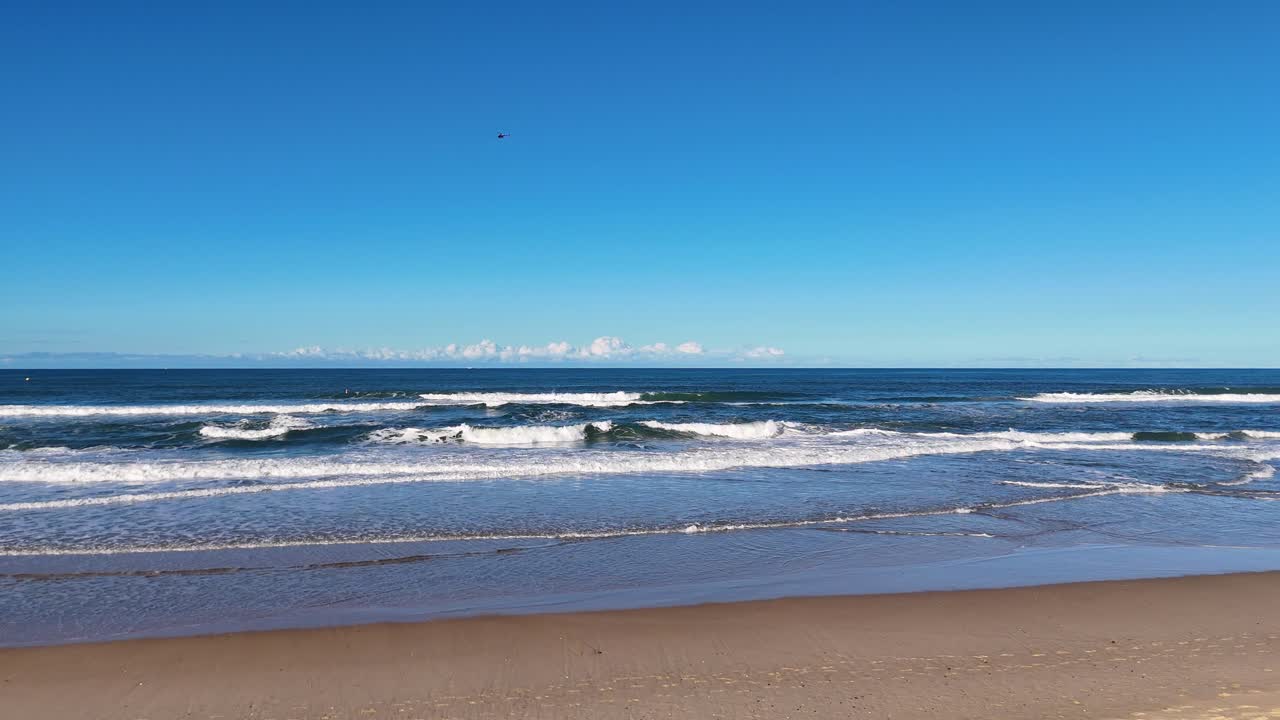 Aerial footage of waves gently rolling onto the sandy shore of Surfers Paradise, Gold Coast, under clear blue skies